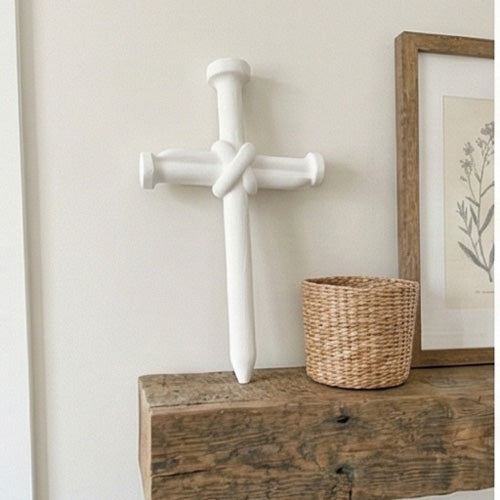 Decorative shelf with a cross of 3 nails art piece next to a basket, and plant against a blue wall.