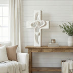 Decorative cross with heart designs on a wooden surface with books and a plant in the background.